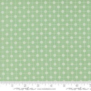 May include: A light green fabric with a repeating pattern of white flowers and grid lines. The fabric has a ruler along the bottom edge, with the word "moda" and the website address "www.modafabrics.com" printed on it.