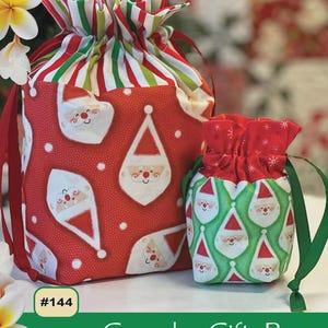 May include: Two goody gift bags with a Christmas theme. The larger bag is red with white Santa Claus faces and white polka dots. The smaller bag is green with Santa Claus faces. The bags have red and green striped tops and red drawstrings. The text "Goody Gift Bags" is visible.