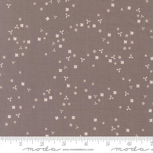 May include: A fabric with a muted brown background, adorned with a delicate pattern of small, off-white floral and star-like shapes. The design is evenly distributed across the surface, creating a subtle, repeating motif. A ruler is at the bottom.
