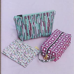 May include: A sewing pattern titled TRIPLIZIP #113 Three Zipper Pouches for Beginners by Jeni Baker. The cover displays three fabric pouches: one with a vertical teal and purple stripe pattern, one with a purple geometric floral print, and one with a multi-colored polka dot pattern.