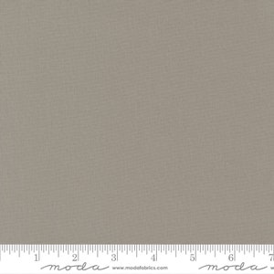 May include: A close-up of a fabric with a neutral, taupe color. The fabric has a subtle woven texture. A ruler is at the bottom of the image, with the word "moda" and the website address "www.modafabrics.com" printed on it. The fabric is suitable for quilting and sewing projects.