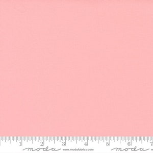 May include: A solid, light pink fabric with a subtle textured surface. A ruler with inch measurements is visible at the bottom of the image. The fabric is likely used for quilting or sewing projects.
