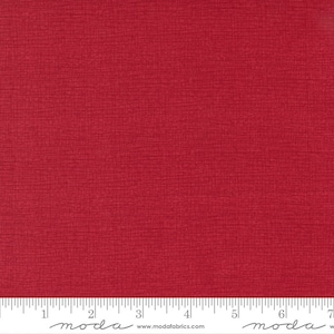 May include: A close-up of a vibrant red fabric with a textured surface. The fabric has a subtle, crosshatch pattern, and a ruler is placed along the bottom edge. The fabric is likely used for quilting or other sewing projects.