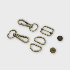 May include: A collection of antique brass-colored hardware components, including two swivel clasps, two D-rings, a rectangular buckle, and two magnetic snap closures. These items are likely for bag making or crafting projects.
