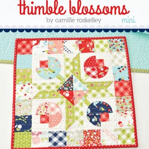May include: A mini quilt with a red border, featuring a patchwork design with floral and geometric patterns in red, green, blue, and white. The quilt is labeled "thimble blossoms" and "Flower Patch #195".