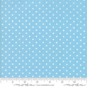 May include: Light blue fabric with a repeating pattern of white polka dots. The fabric is marked with a ruler along the bottom edge, with the brand name "moda" printed at the bottom.
