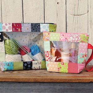 May include: Two patchwork fabric pouches with clear vinyl windows. One contains yarn and knitting needles, the other toiletries. The pouches are made of colorful fabric squares and have zippers. The larger pouch is approximately 10 inches wide.