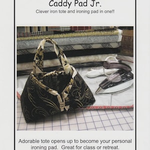 May include: A Sisters' Common Thread Caddy Pad Jr. product label featuring a black and gold patterned fabric tote that unfolds into an ironing pad. The text includes 'Caddy Pad Jr.' and 'Sized to hold your 6"-8 1/4" travel iron.'