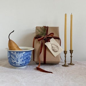 hand painted pear on linen tag on a gift beside two candles and a blue bowl