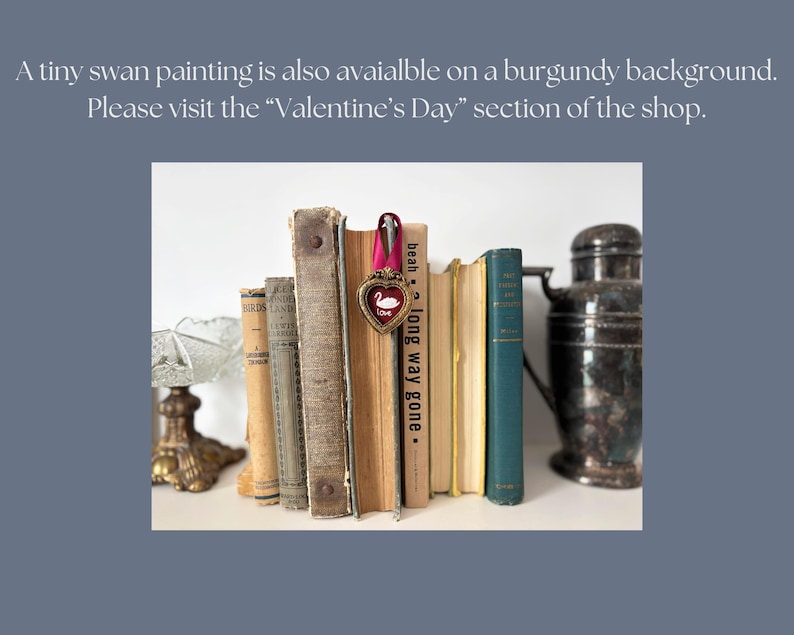 May include: A collection of vintage books with aged covers, some with visible titles. A heart-shaped ornament with a swan design hangs from a pink ribbon. A decorative metal container is on the right. The text in the image says: "A tiny swan painting is also available on a burgundy background."