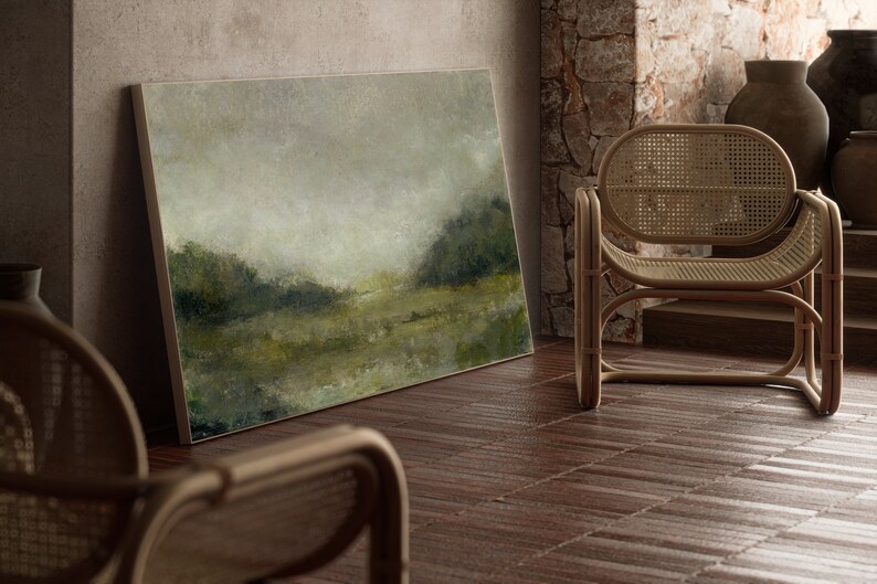 A thin wooden frame holds a vintage landscape oil painting. The art is leaning against a stone wall beside modern cane chairs.