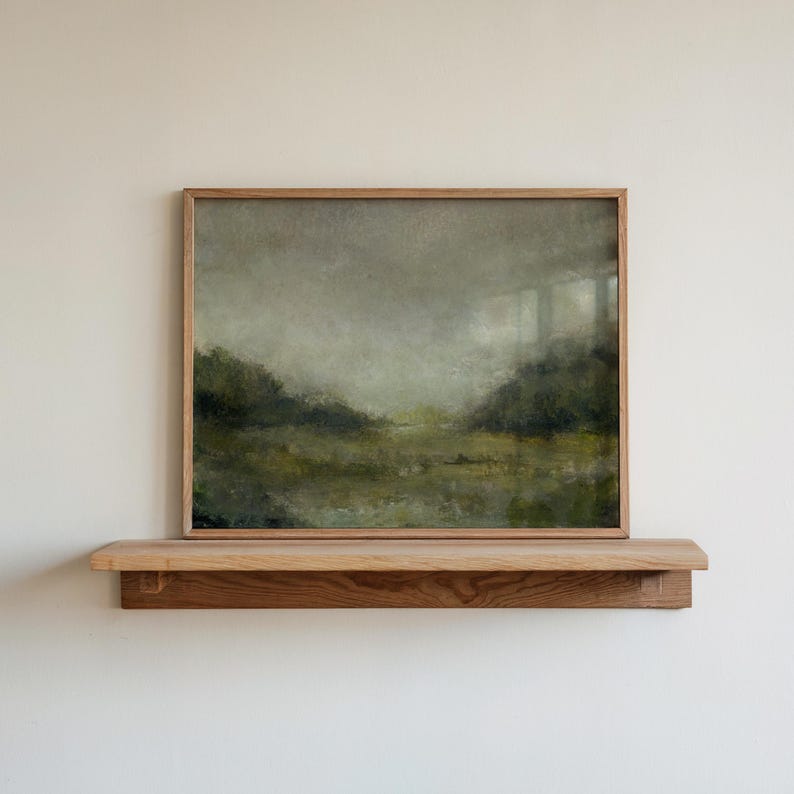 A wooden frame holds a vintage landscape oil painting on a wooden shelf against a white wall.