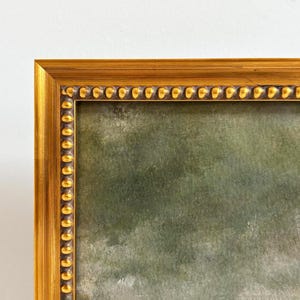 The top left corner of a gold frame  with beading and a fine art landscape art print.