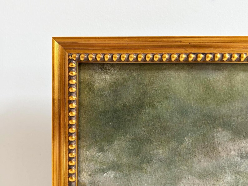 The top left corner of a gold frame  with beading and a fine art landscape art print.