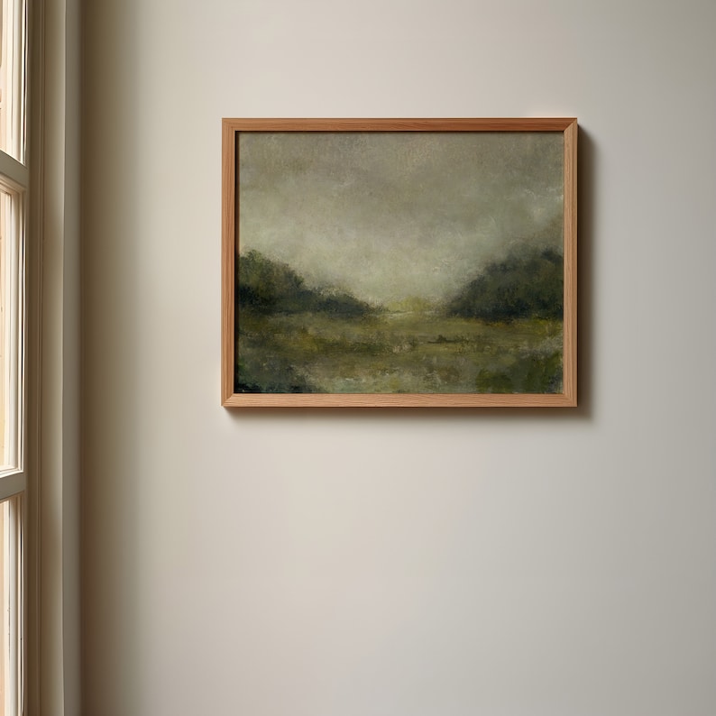 A wooden frame holds a vintage landscape oil painting on a white wall beside a window.