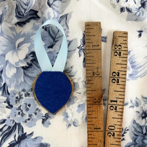 The back of a tiny framed painting in a heart-shaped vintage gold frame with pale blue ribbon and royal blue felt, displayed on blue and white roses, romantic cottagecore decor.