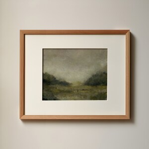 A wooden frame with a white mat holds a vintage landscape oil painting on a white wall.