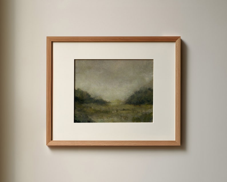 A wooden frame with a white mat holds a vintage landscape oil painting on a white wall.