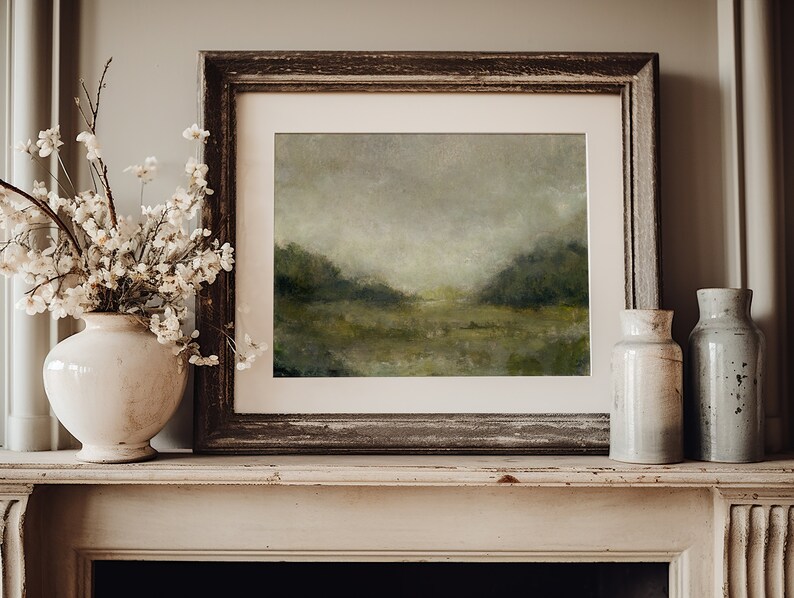 May include: A framed landscape painting of a misty green field with a wooden frame on a white mantelpiece with two ceramic vases.