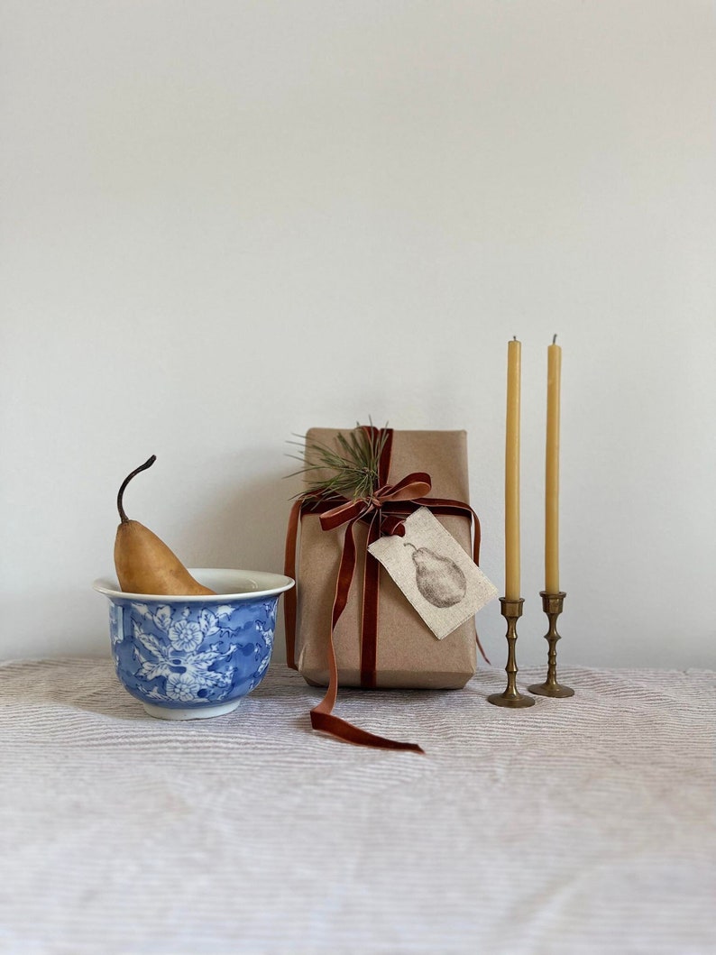 hand painted pear on linen tag on a gift beside two candles and a blue bowl