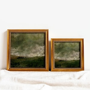 2 gold frames with beading frames a vintage English countryside landscape art print. The frames are sitting on beige fabric with a white wall in the background.