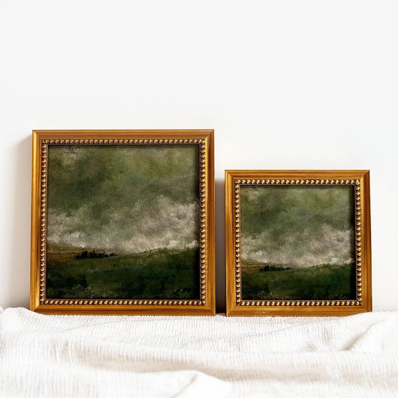 2 gold frames with beading frames a vintage English countryside landscape art print. The frames are sitting on beige fabric with a white wall in the background.