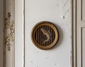 May include: A round, framed artwork featuring a fish. The fish is depicted in a realistic style, with a brown and beige color palette. The frame is gold-toned, and the background is a dark brown with vertical lines.