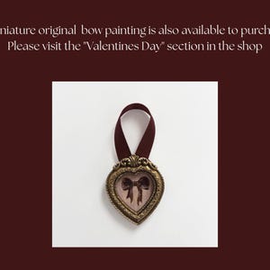 May include: A heart-shaped, antique-style frame with a bow painting inside, suspended by a maroon ribbon. The frame has an ornate, gold-colored border. The text in the image says, "A miniature original bow painting is also available to purchase. Please visit the "Valentines Day" section in the shop."