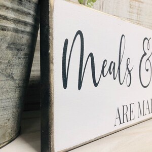 May include: White wooden sign with black text that reads "Meals & are made with love". The sign has a distressed, rustic look.