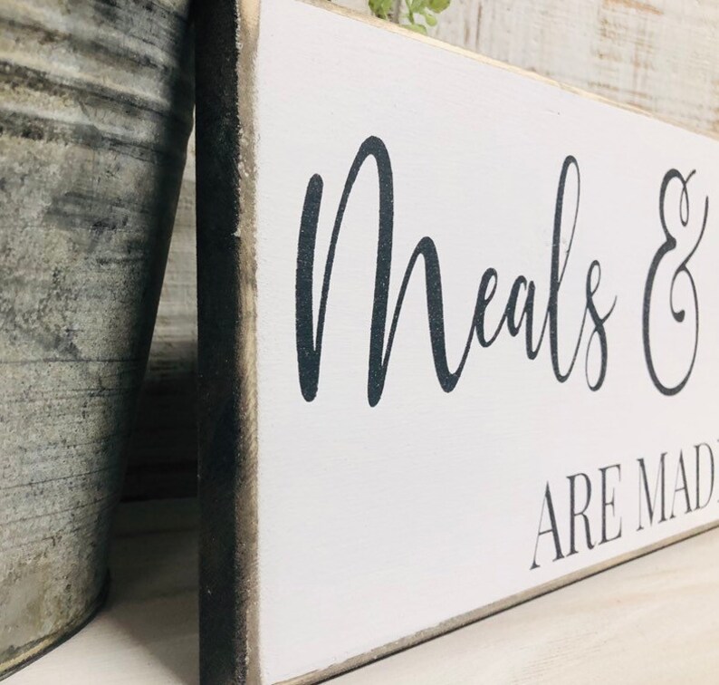 May include: White wooden sign with black text that reads "Meals & are made with love". The sign has a distressed, rustic look.