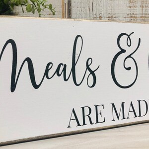 May include: White wooden sign with black calligraphy that reads "Meals & Memories Are Made Here".