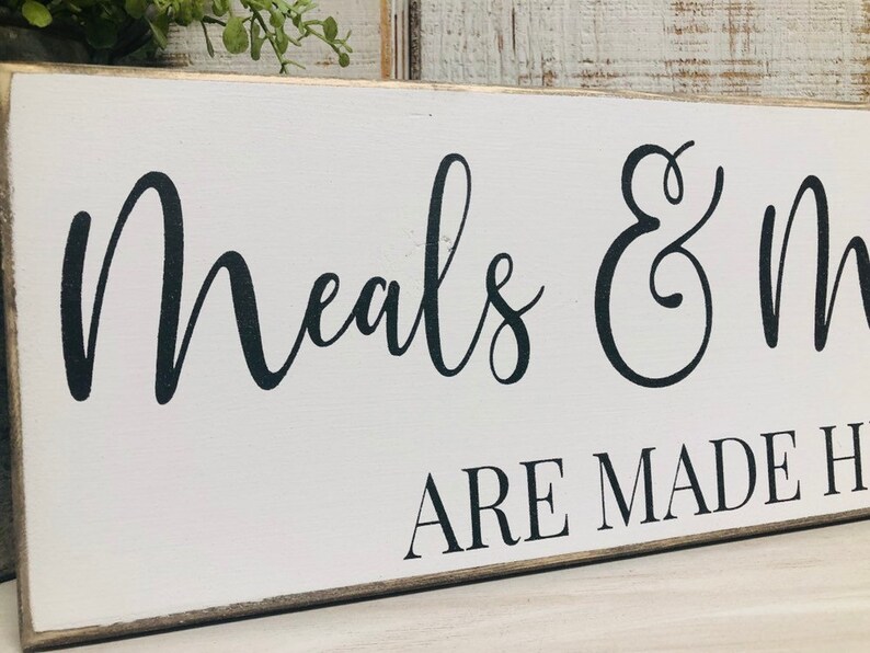 May include: White wooden sign with black calligraphy that reads "Meals & Memories Are Made Here".