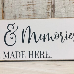 May include: White wooden sign with black cursive text that reads "Smiles & Memories Are Made Here."