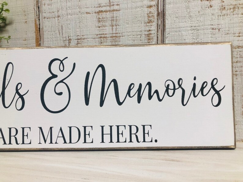 May include: White wooden sign with black cursive text that reads "Smiles & Memories Are Made Here."
