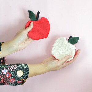 May include: Two fabric apple-shaped hand warmers. One is red with green leaves and the other is white with green leaves.
