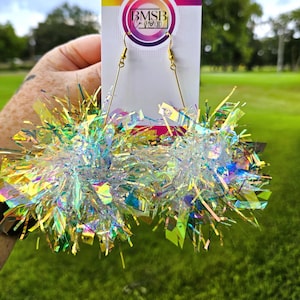 May include: Iridescent, multi-colored earrings with gold-colored hooks. The earrings are made of shiny, reflective material, creating a sparkling effect. The earrings are displayed on a white card with a logo that reads "BMSB".