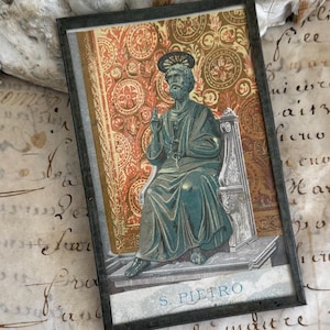 May include: A framed image featuring a seated figure in teal robes, with a halo, against a patterned background of red and gold. The image is labeled "S. Pietro" and is set in a dark frame. The background includes aged paper with handwritten script.