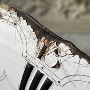 May include: Close-up of a white ceramic plate with black and brown accents. The plate features a cracked surface, black vertical stripes, and a decorative design with the number 16. The rim is dark brown.