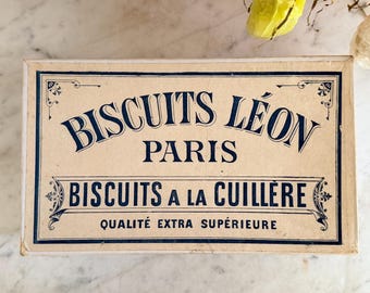 May include: Vintage rectangular box with the text "BISCUITS LÉON PARIS BISCUITS A LA CUILLÈRE QUALITÉ EXTRA SUPÉRIEURE" in navy blue on a cream background. The box has decorative navy blue borders and accents.