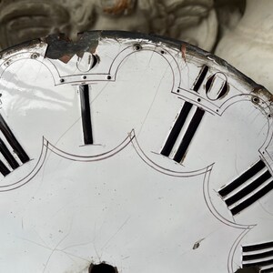 May include: Close-up of a vintage clock face with Roman numerals. The white face has black Roman numerals and black lines. The clock face is damaged, with cracks and missing pieces around the edges. The numerals are in black.