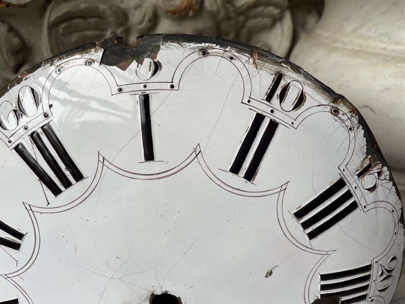 May include: Close-up of a vintage clock face with Roman numerals. The white face has black Roman numerals and black lines. The clock face is damaged, with cracks and missing pieces around the edges. The numerals are in black.