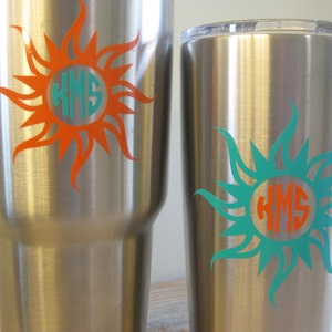 May include: Two stainless steel tumblers with a sun design and the monogram "KMS" in a circle. The sun on the left tumbler is orange and the sun on the right tumbler is teal.
