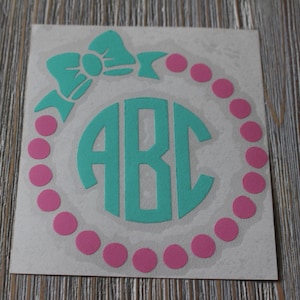 May include: A teal monogram decal with the letters "ABC" surrounded by a pink polka dot circle. A teal bow is above the monogram.