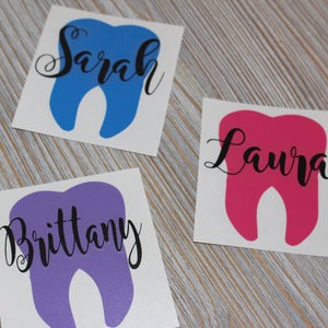 Op de afbeelding: Drie tanden-vormige stickers met namen erop. De stickers zijn blauw, roze en paars. De namen zijn "Sarah", "Laura" en "Brittany".