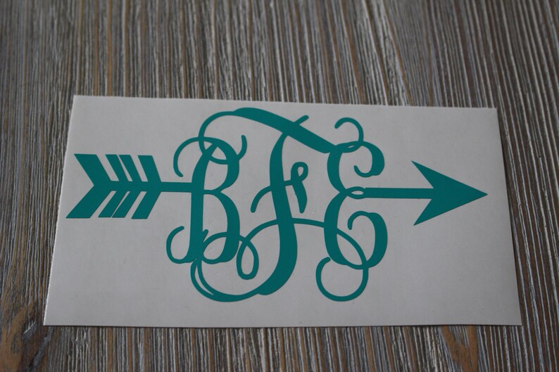 Op de afbeelding: Tealblauwe vinyl sticker met een monogram van de letters "B F G" in een cursief schrift. Het monogram is gecentreerd op een pijl die naar rechts wijst.