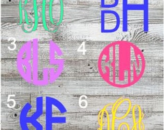 May include: Six different monogram designs on a wood background. The monograms are in various colors and styles, including script, block, and circle.