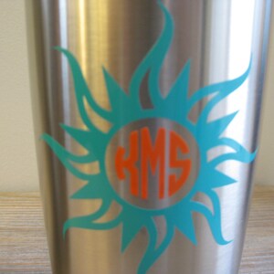 May include: A stainless steel tumbler featuring a turquoise sunburst design and a monogram in an orange circle. The monogram reads "KMS".