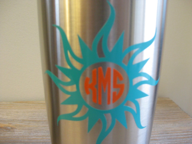 May include: A stainless steel tumbler featuring a turquoise sunburst design and a monogram in an orange circle. The monogram reads "KMS".