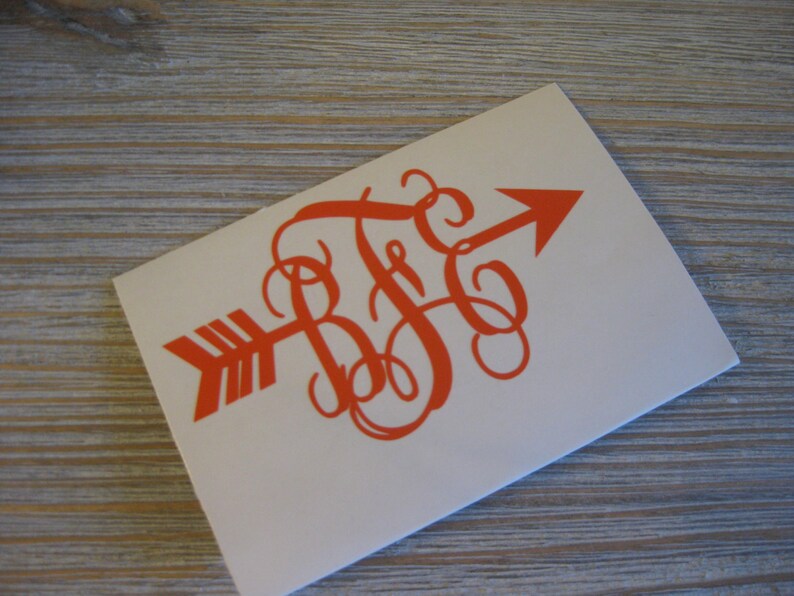 Op de afbeelding: Oranje vinyl sticker met een monogram van de letters "B F G" in een schrijfletter, met een pijl die naar rechts wijst.
