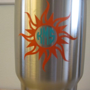 May include: A stainless steel tumbler featuring an orange sun design with a turquoise monogram "KMS" in the centre.